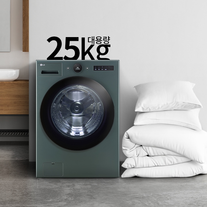 세탁기가 놓여 있으며, 그 위에 25kg 대용량이라는 문구가 있습니다. 세탁기 옆에는 하얀색 베개와 이불이 쌓여 있고, 배경에는 세면대와 거울이 있는 깔끔한 인테리어가 보입니다.