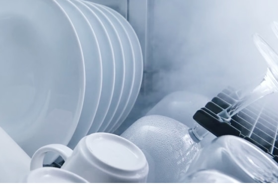 식기세척기 내부의 흰색 접시, 컵, 그리고 물방울이 맺힌 유리잔의 근접 사진으로, 수증기가 식으며 건조되는 모습입니다.