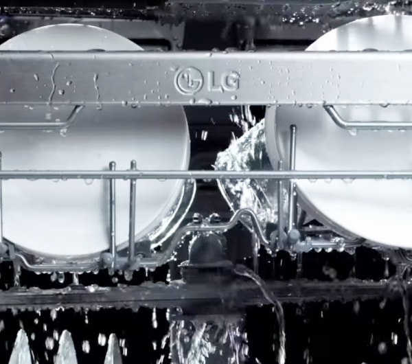 식기세척기 내부에서 물이 뿌려지고, 상단 선반에 놓여 있는 접시와 유리잔에 물방울이 맺혀 있는 모습.