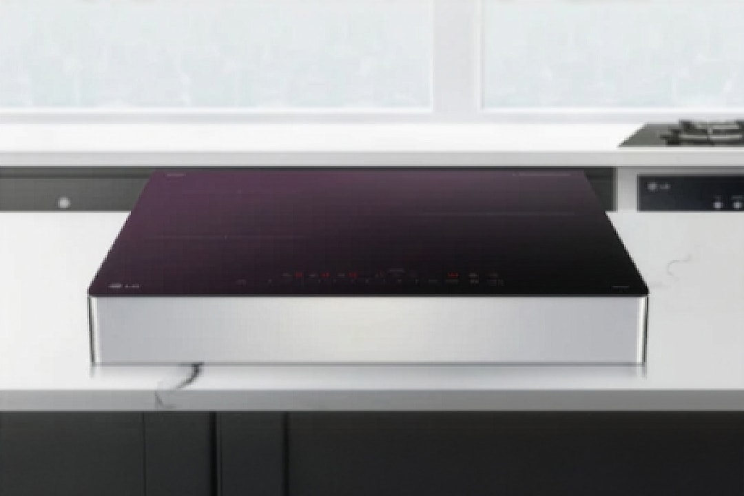 은색 프레임으로 마감된 인덕션이 주방 조리대 위에 안정적으로 놓여 있으며, 상판은 검은색 글라스 소재로 원형·십자 형태의 조리 구역과 화력, 타이머, 잠금 등의 터치 아이콘이 선명하게 표시되어 있습니다.