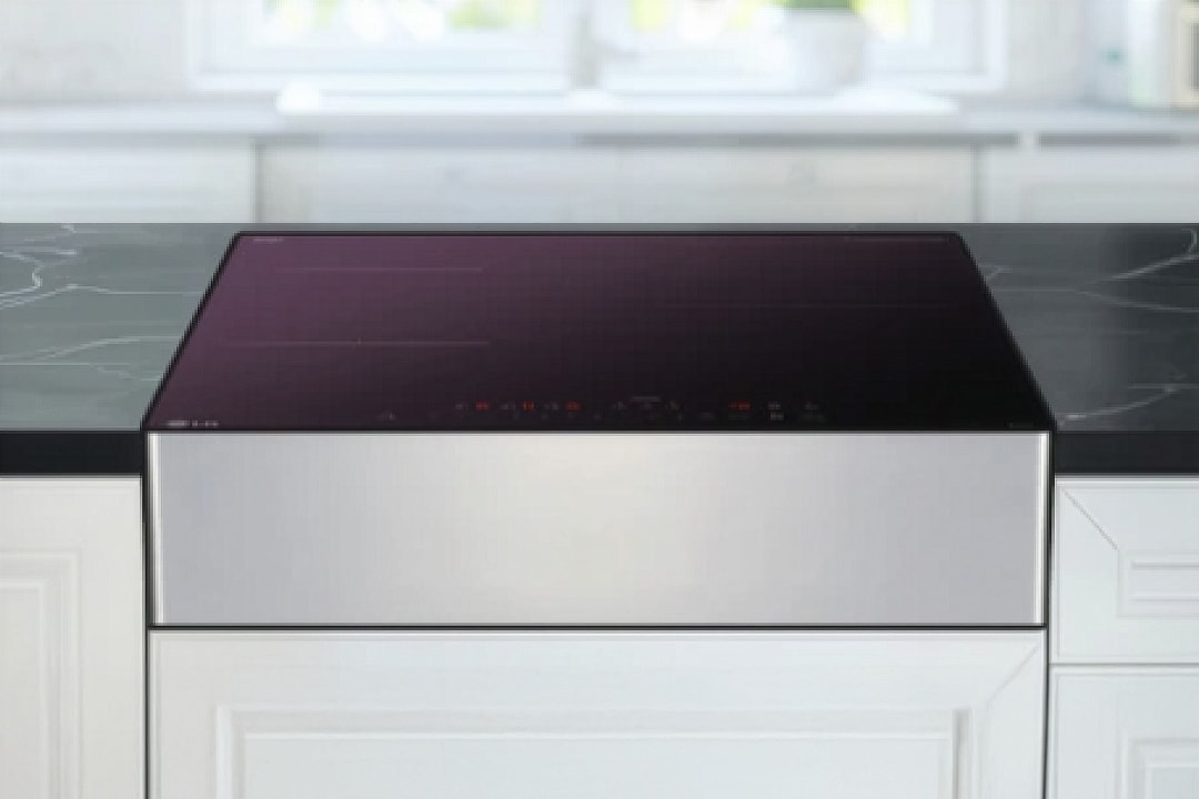 은색 프레임으로 마감된 인덕션이 주방 조리대 위에 안정적으로 놓여 있으며, 상판은 검은색 글라스 소재로 원형·십자 형태의 조리 구역과 화력, 타이머, 잠금 등의 터치 아이콘이 선명하게 표시되어 있습니다.