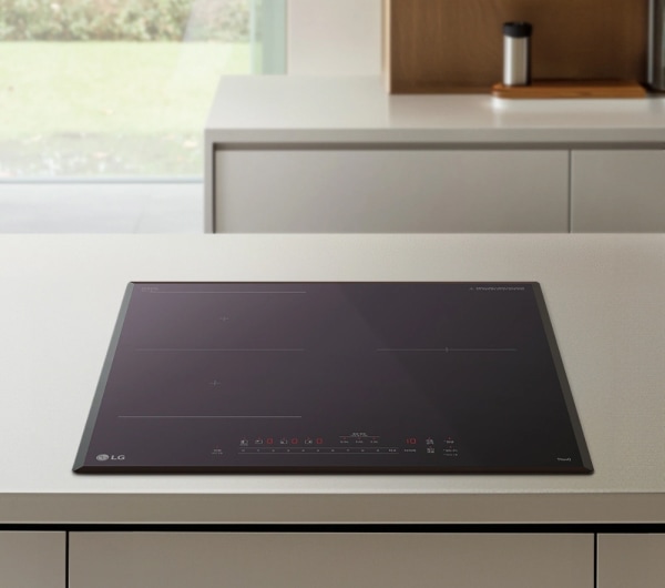 밝은 톤의 조리대 위에 블랙 컬러의 인덕션이 매립형으로 설치되어 있습니다. 배경에는 넓은 창으로 자연 풍경이 들어오고, 간결한 수납장과 소품이 함께 보여 모던한 주방 분위기를 연출하는 이미지입니다.