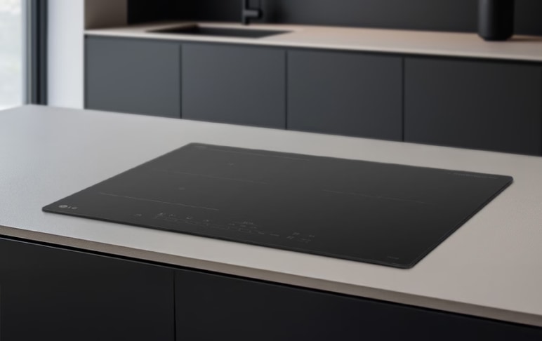 검은색 인덕션이 밝은 색상의 주방 조리대에 설치되어 있습니다. 인덕션 표면에는 다양한 조작 버튼과 기능 표시가 있으며, 주변은 모던한 디자인의 주방 가구로 구성되어 있습니다.