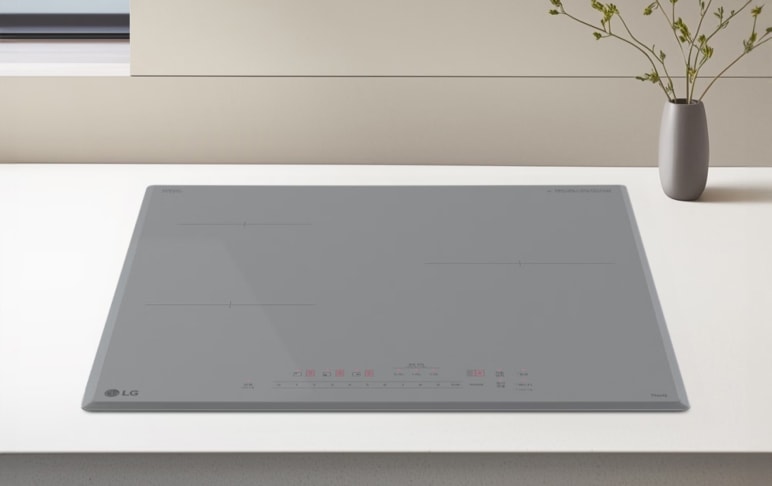 밝은 톤의 조리대 위에 연한 그레이 색상의 인덕션이 매립형으로 설치되어 있습니다. 상판에는 직선 형태의 조리 구역 표시와 전원, 화력, 타이머 등의 터치 아이콘이 은은한 붉은빛으로 정렬되어 있습니다. 배경에는 간결한 수납장과 작은 화병이 놓여 있어, 차분하고 미니멀한 주방 분위기를 연출합니다.