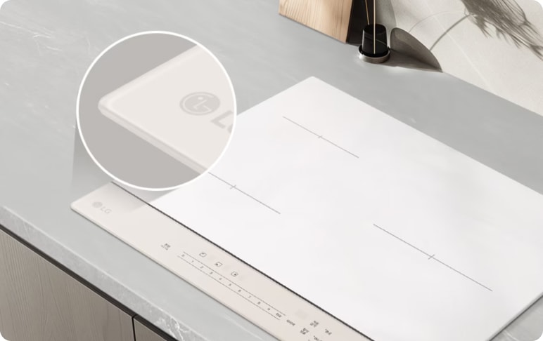 밝은 그레이 톤의 조리대 위에 화이트 색상의 인덕션이 매립형으로 설치되어 있습니다. 상판 모서리를 확대해 보여주는 원형 인셋 이미지가 함께 구성되어 제품의 마감 디테일을 강조합니다. 