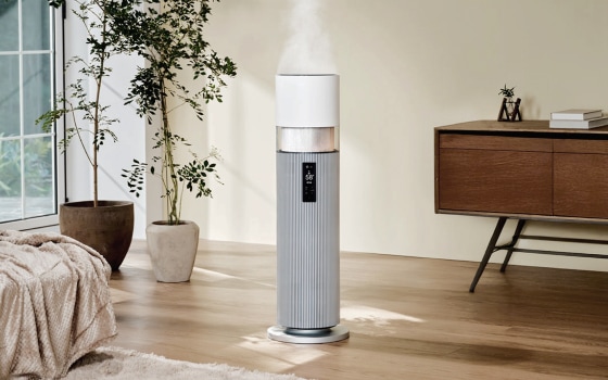 밝은색 실내에 위치한 LG 퓨리케어 하이드로타워 가습기로, 상단에서 수증기가 분사되고 있으며, 전면에 디지털 디스플레이가 보입니다.