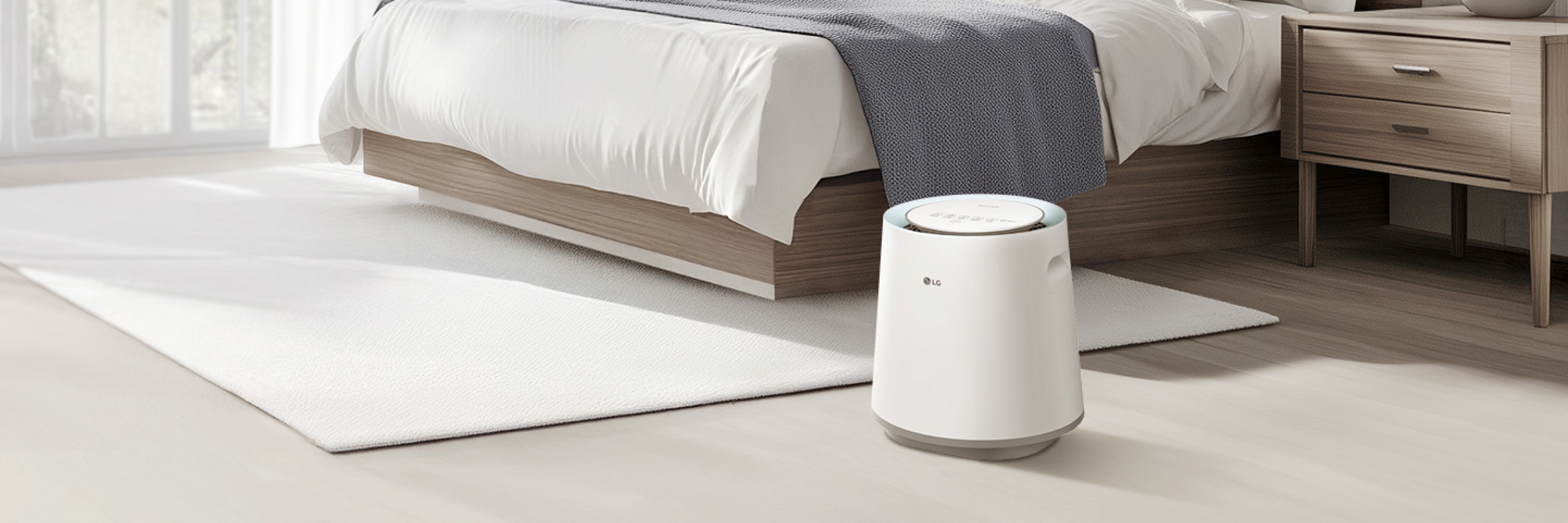 침실에 놓인 LG 퓨리케어 자연 기화 가습기로, 흰색 침구와 베개, 나무 질감의 침대 프레임 옆 흰색 러그 위에 놓여 있습니다.