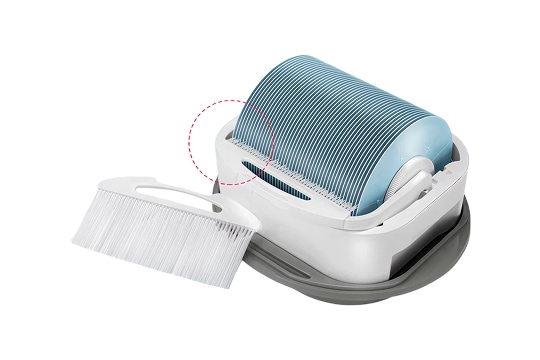 회색과 흰색의 플라스틱 소재로 된 고양이 화장실이 있으며, 둥근 모양의 파란색 필터가 장착되어 있습니다. 옆에는 흰색 손잡이가 달린 브러시가 놓여 있습니다. 배경은 단색으로 깔끔하게 처리되어 있습니다.