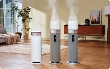 거실 바닥에 놓인 하이드로에센셜 제품 1개와 회색 하이드로타워 제품 2개가 가동 중이며, 각 제품 위에서 흰 수증기가 분사되고 있습니다.