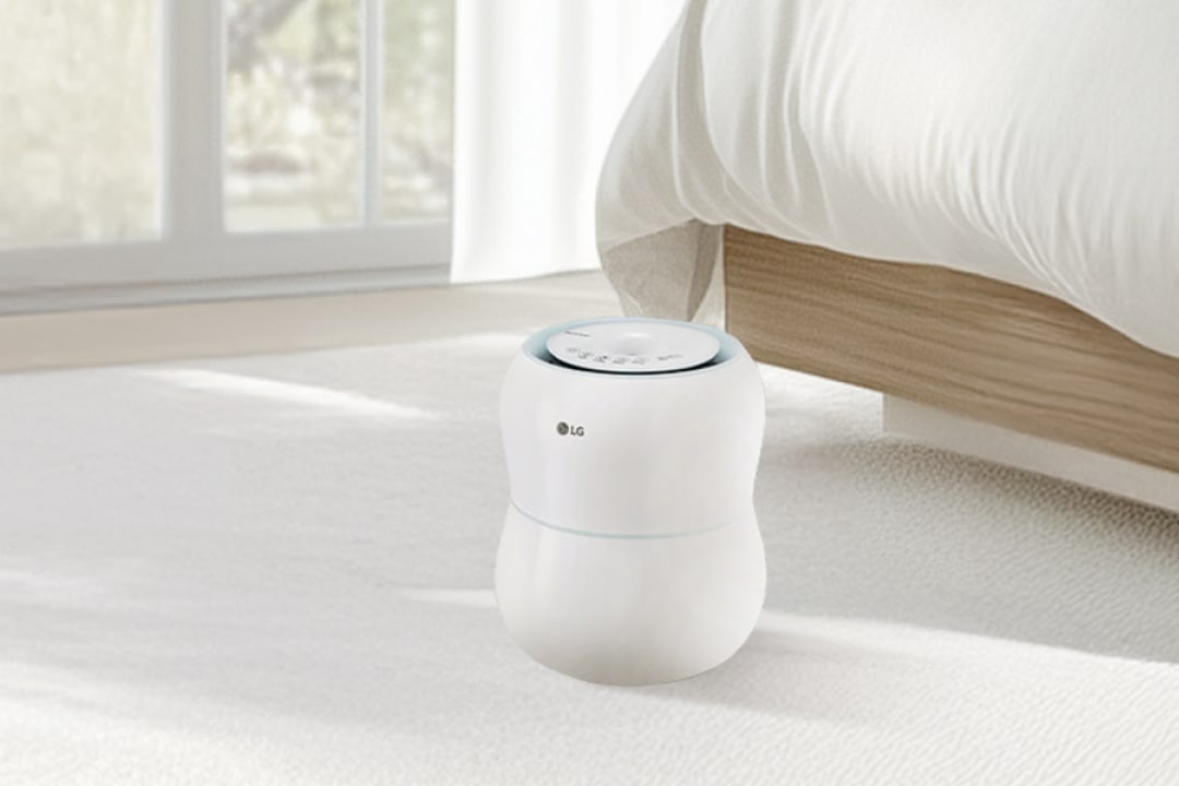 침실 배경에 흰색 LG 가습기가 베이지색 침대 앞 흰색 카펫 위에 놓여 있습니다.