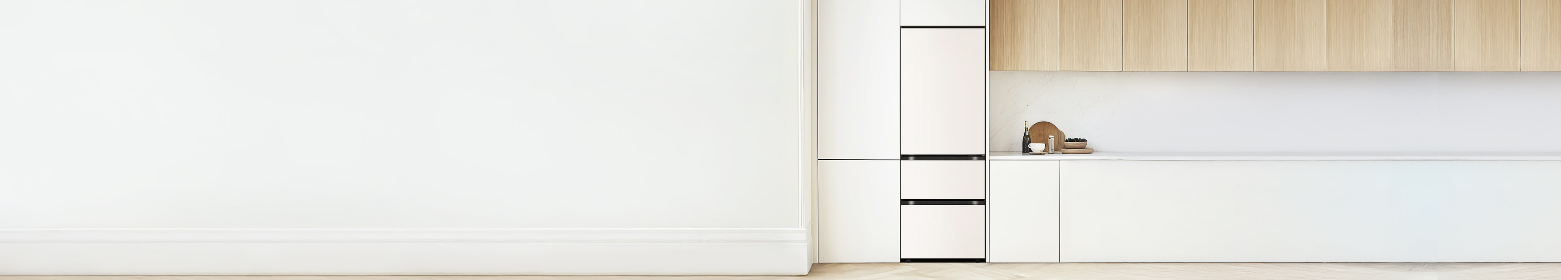 빌트인 구조의 매트 화이트 김치냉장고가 설치되어 있습니다. 그 오른쪽에는 흰색 하부장과 연한 원목 상부장이 조화를 이루고 있으며, 조리대 위에는 와인 병, 컵, 그릇, 나무 도마 등이 깔끔하게 배치되어 있습니다.