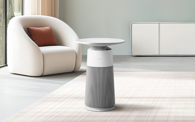 밝은 색상의 거실 배경에 흰색 1인 쇼파와 LG 퓨리케어 AI 오브제컬렉션 에어로퍼니처 제품이 배치되어 있습니다. 공기청정기는 테이블 형태의 흰색 디자인이며 바닥에 놓여져 있습니다. 뒤쪽에는 흰색 캐비닛이 위치해 있습니다.