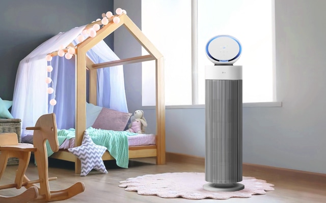 어린이 방에 LG 퓨리케어 오브제컬렉션 에어로부스터가 놓여있습니다. 방 안에는 나무 프레임으로 된 침대, 나무 흔들 목마, 라탄 바구니, 별 모양 쿠션 등이 놓여져 있습니다. 공기청정기는 흰색과 회색으로 이루어져 있으며, 윗부분 원형 디스플레이에 파란색 빛이 들어와 있습니다. 바닥에는 옅은 분홍색 러그가 깔려 있습니다.