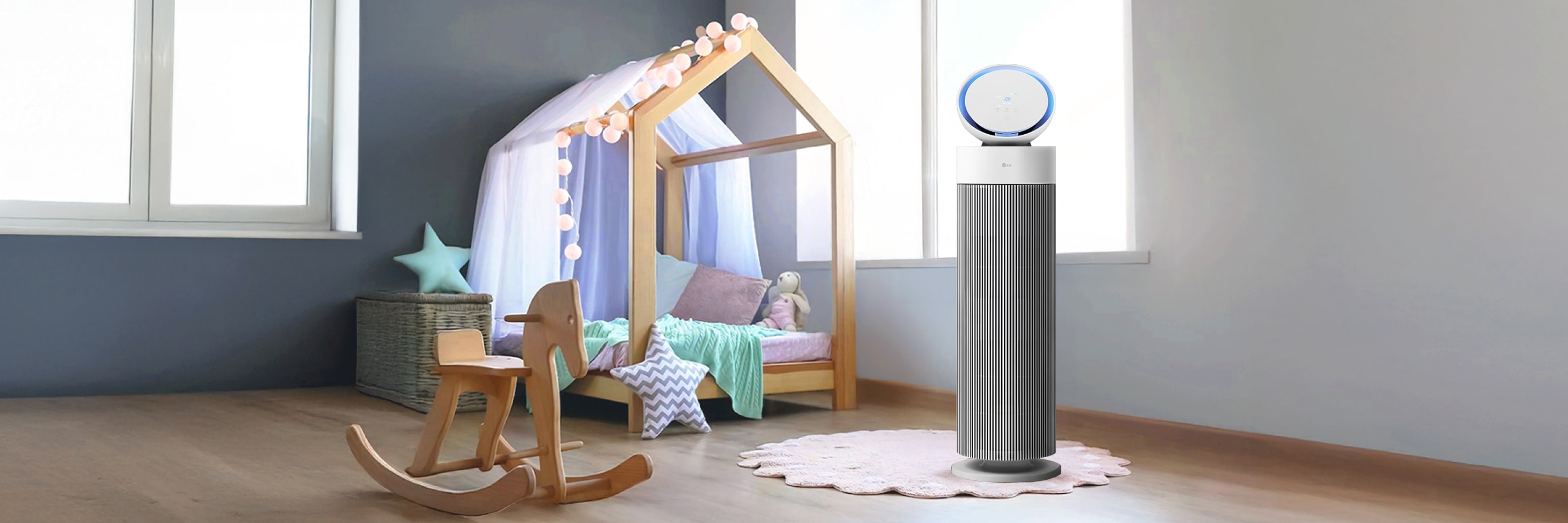 어린이 방에 LG 퓨리케어 오브제컬렉션 에어로부스터가 놓여있습니다. 방 안에는 나무 프레임으로 된 침대, 나무 흔들 목마, 라탄 바구니, 별 모양 쿠션 등이 놓여져 있습니다. 공기청정기는 흰색과 회색으로 이루어져 있으며, 윗부분 원형 디스플레이에 파란색 빛이 들어와 있습니다. 바닥에는 옅은 분홍색 러그가 깔려 있습니다.