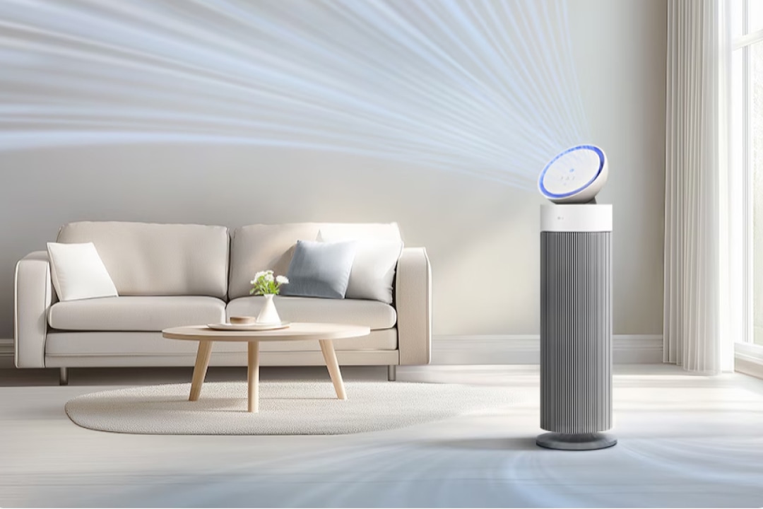 밝은 자연광이 드는 거실에 LG 퓨리케어 오브제컬렉션 에어로부스터가 세워져 있으며, 상단 원형 헤드에서 부드러운 바람이 퍼져나가는 모습이 표현되어 있습니다. 미니멀한 소파와 우드 테이블이 놓인 깔끔한 공간과 조화를 이루며 편안하고 쾌적한 분위기를 연출합니다.