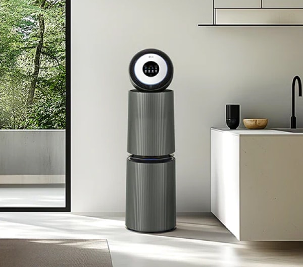 주방 공간에 공기청정기가 놓여 있고, 싱크대와 수납장이 있습니다. 큰 창문을 통해 자연광이 들어오고 있으며, 녹색 나무가 보입니다.