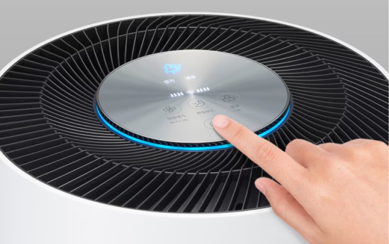 공기청정기 상단에 디스플레이 버튼을 손으로 누르고 있습니다. 공기의 질이 좋음을 나타내는 파란색 청정표시등이 켜져있습니다.