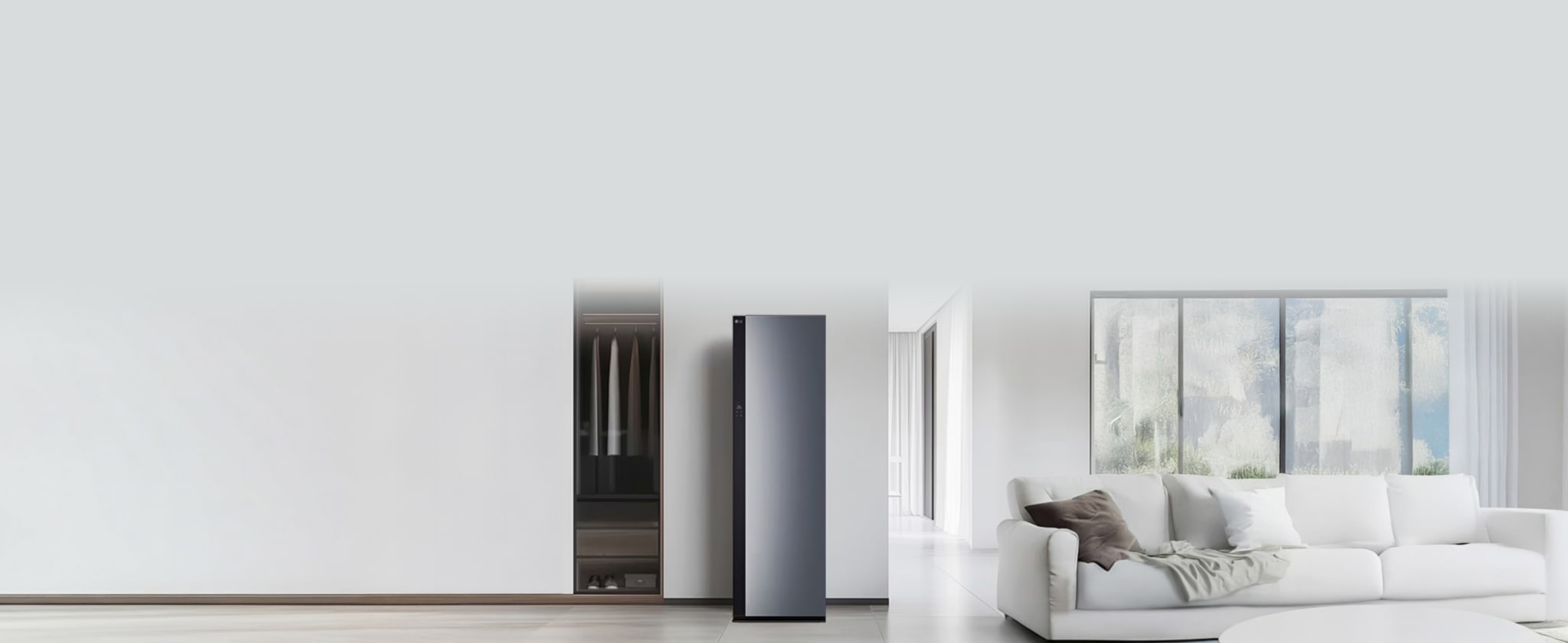 깔끔한 집 내부 공간 가운데 그레이 계열 색상의 스타일러가 놓여져있습니다. 왼쪽에는 옷장과 정갈하게 걸려져있는 옷들, 오른쪽에는 편안한 분위기의 소파와 거실 공간이 보여집니다.