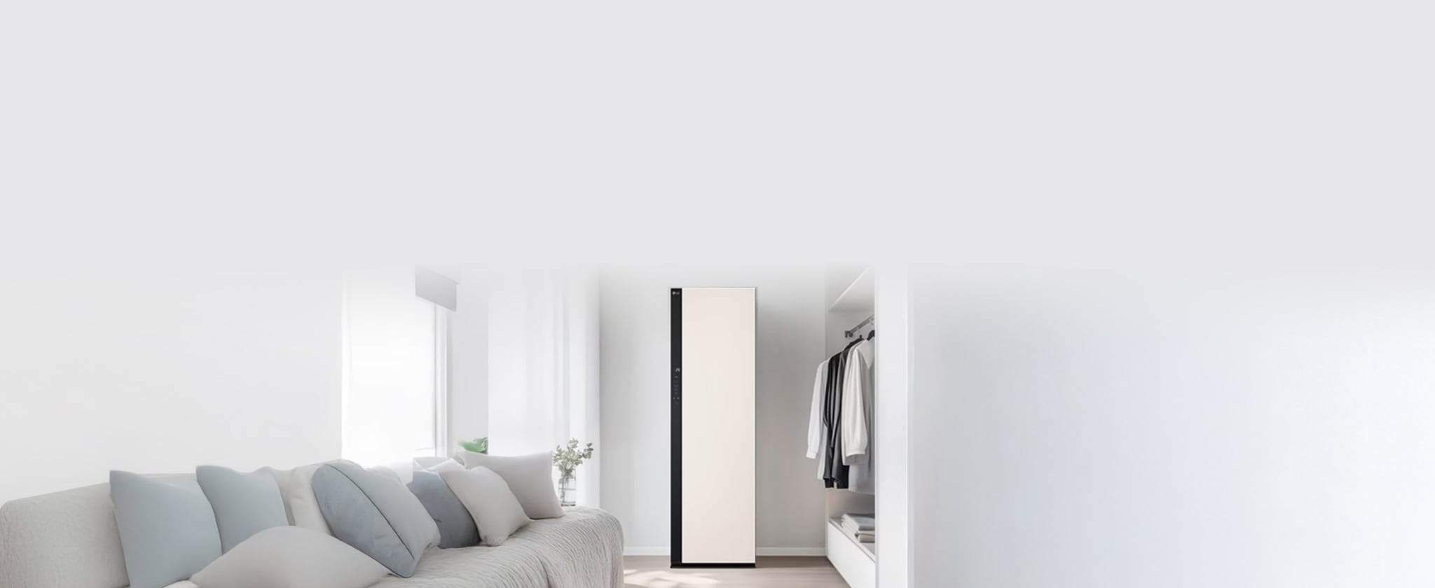 화이트 톤의 드레스룸 안에 정갈하게 걸려있는 옷가지들과 밝은 스타일러가 함께 배치되어있습니다. 왼쪽 공간에는 창문과 소파가 놓여져있습니다.