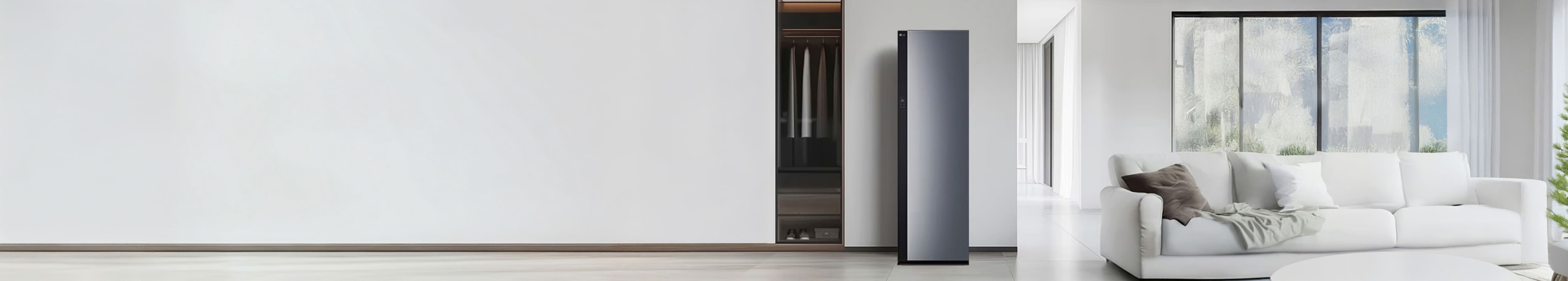 깔끔한 집 내부 공간 가운데 그레이 계열 색상의 스타일러가 놓여져있습니다. 왼쪽에는 옷장과 정갈하게 걸려져있는 옷들, 오른쪽에는 편안한 분위기의 소파와 거실 공간이 보여집니다.