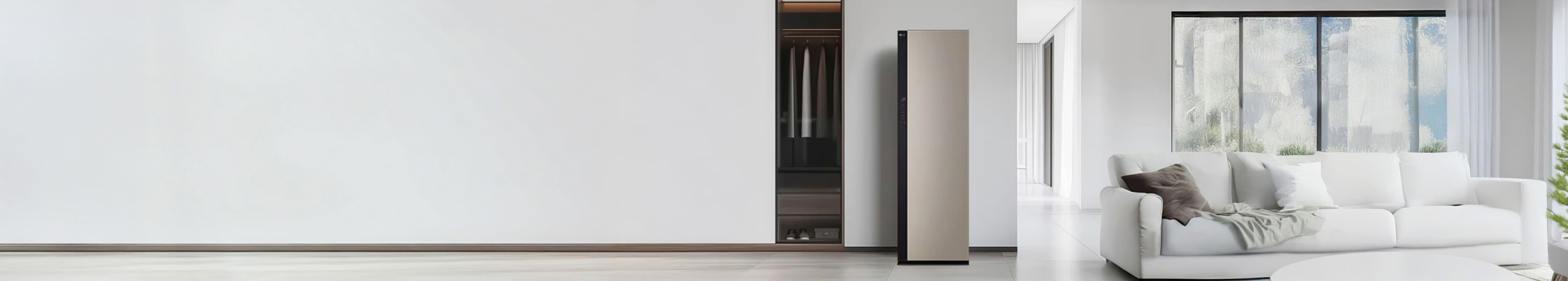 깔끔한 집 내부 공간 가운데 베이지 계열 색상의 스타일러가 놓여져있습니다. 왼쪽에는 옷장과 정갈하게 걸려져있는 옷들, 오른쪽에는 편안한 분위기의 소파와 거실 공간이 보여집니다.