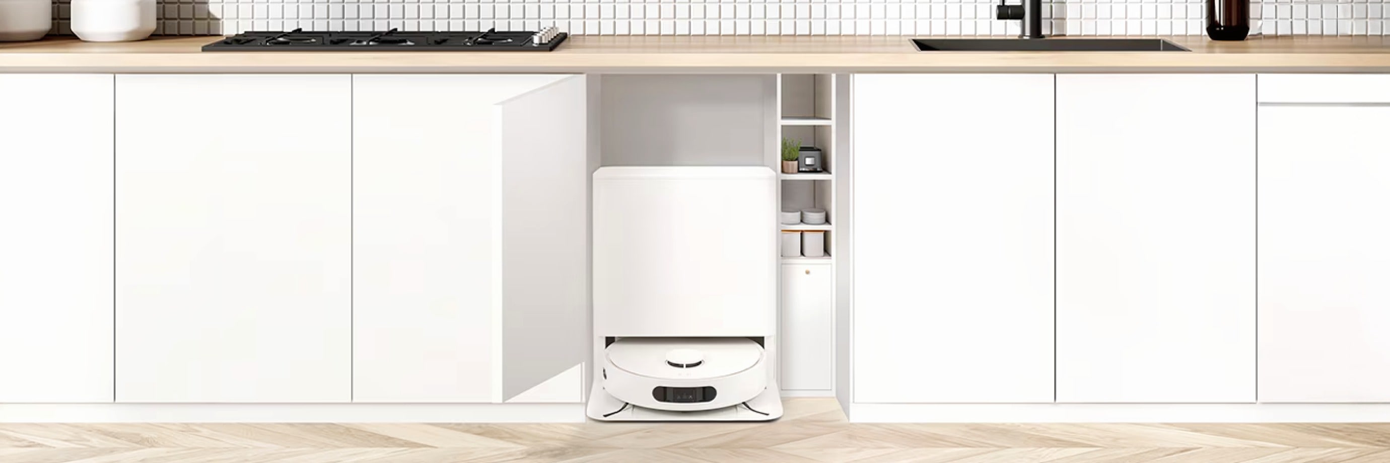 회색 하부장이 있는 깔끔한 주방으로, 한 하부장 문이 열려 흰색 청소 로봇과 충전 스테이션이 보입니다.