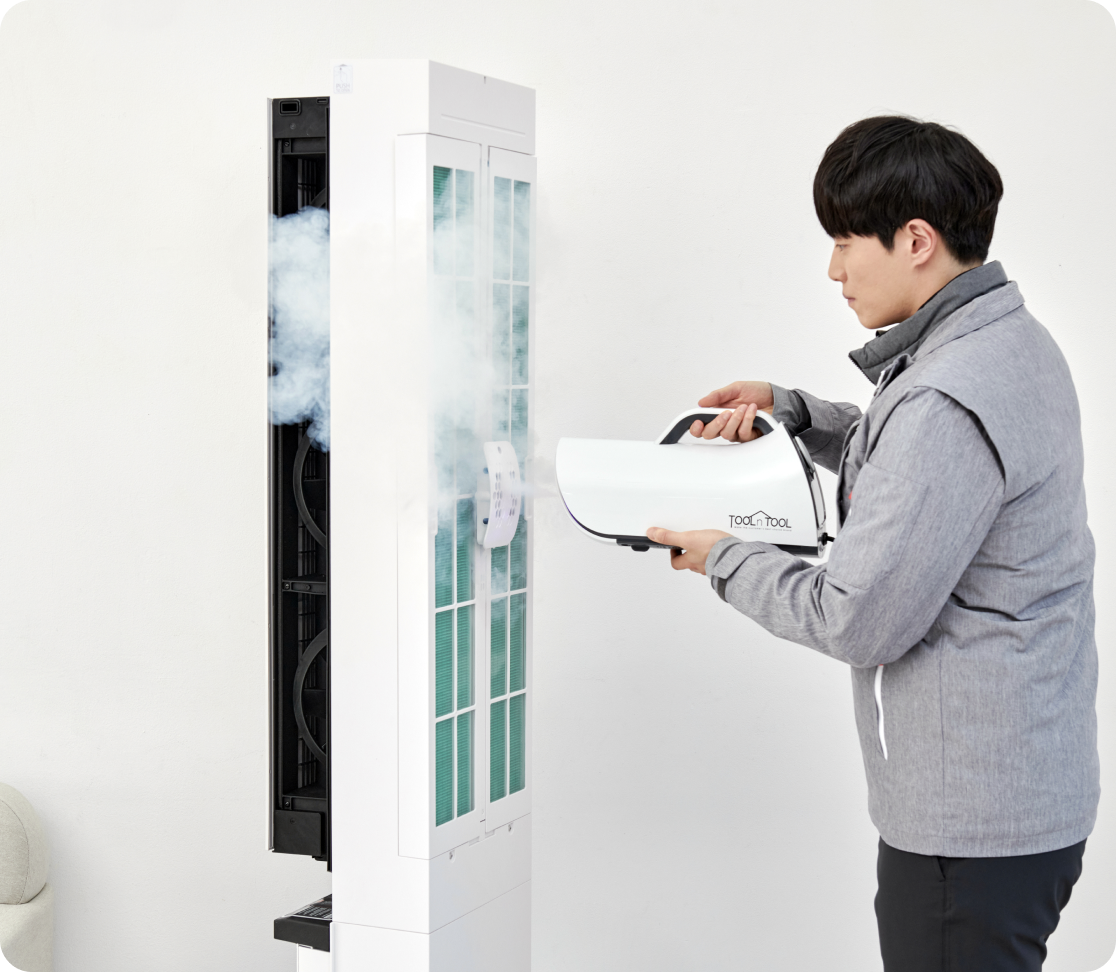 전문가가 LG 스탠드형 에어컨 내부를 전용 장비로 스팀 살균 중. 에어컨에서 흰색 증기가 퍼지며 위생 관리 과정이 진행됨.
