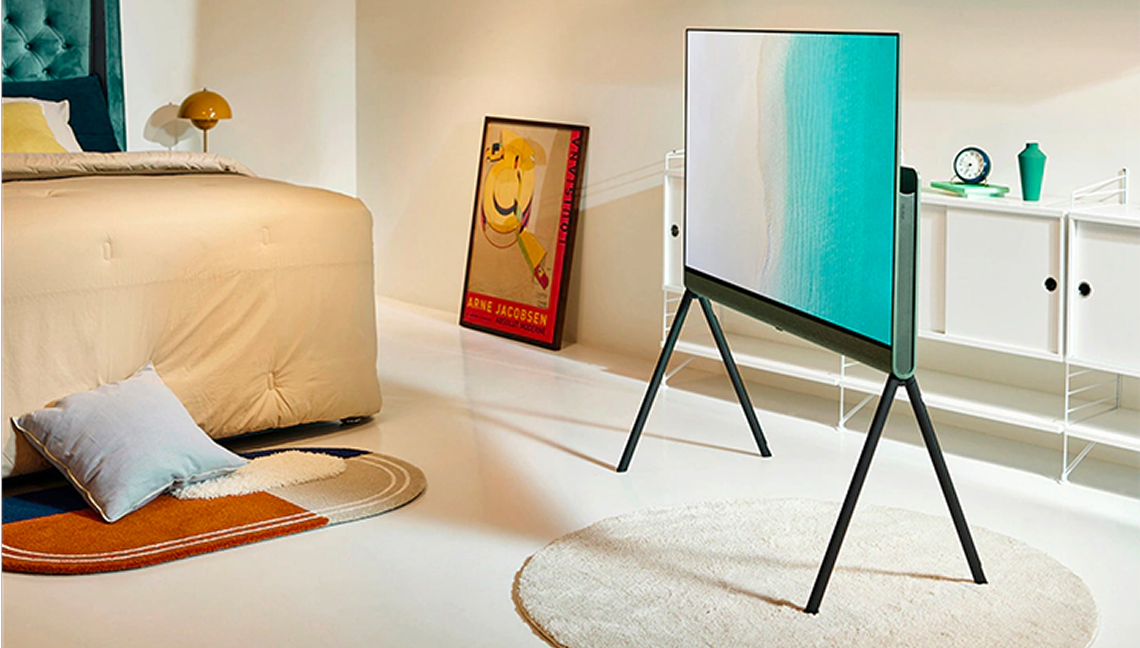 침실 공간에 스탠드형으로 설치된 LG TV, 화면에는 푸른빛 바다가 표현되어 있고, 주변에는 침대와 인테리어 소품이 배치된 모습.