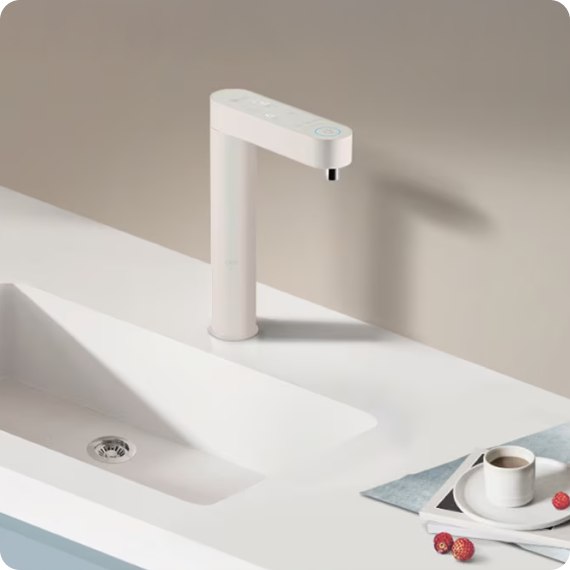 화이트 톤의 빌트인 정수기가 주방 싱크대 위에 설치된 모습. 커피잔과 라즈베리 몇 알이 놓인 접시가 함께 배치되어 있다.