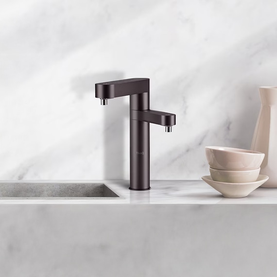 하얀 대리석 느낌의 싱크대. 블랙 색상의 듀얼 정수기가 설치되어 있고, 옆에는 도자기 잔들과 병이 놓여있다.