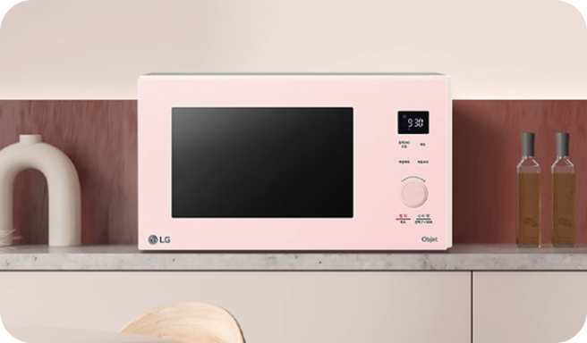 주방 조리대 위에 놓인 LG 오브제컬렉션 핑크색 전자레인지가 우드톤 인테리어와 조화를 이루는 모습.