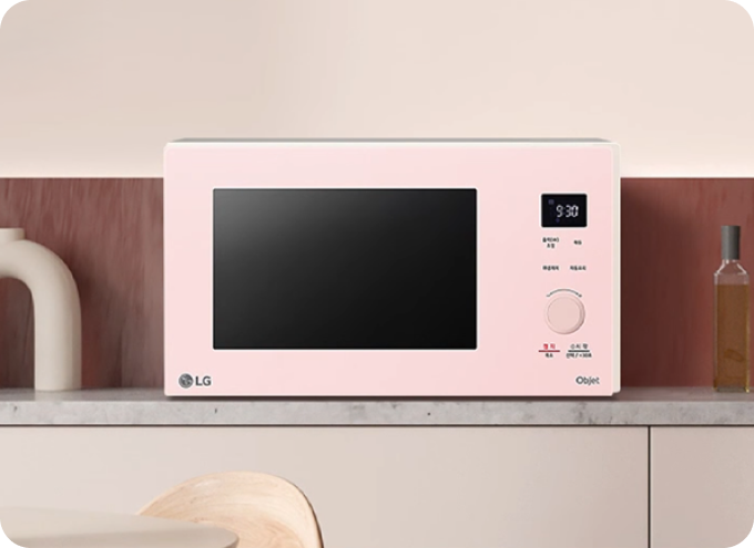 주방 조리대 위에 놓인 LG 오브제컬렉션 핑크색 전자레인지가 우드톤 인테리어와 조화를 이루는 모습.