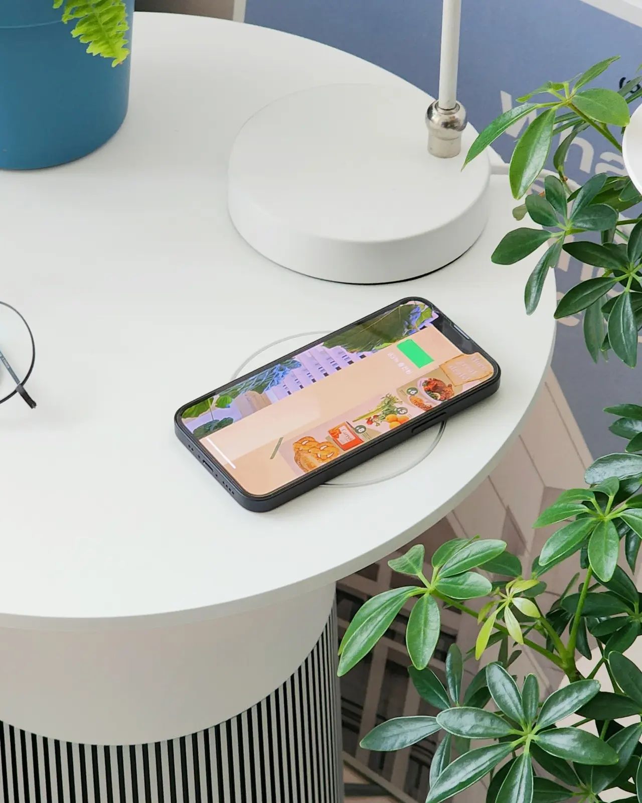 LG 퓨리케어 오브제컬렉션 에어로퍼니처가 화이트 테이블 형태로 사용되고 있다. 테이블 위에는 스마트폰과 안경이 놓여 있으며, 주변에는 초록색 식물이 배치되어 자연스러운 분위기를 연출한다.