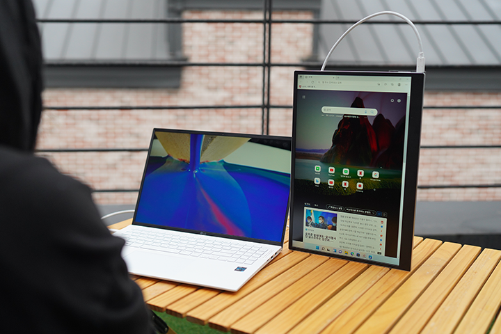 LG 그램 노트북과 그램+view 포터블 듀얼 모니터가 실외 테이블 위에 나란히 놓여 있으며, 모니터는 세로로 배치되어 웹 브라우저 화면을 보여주는 모습