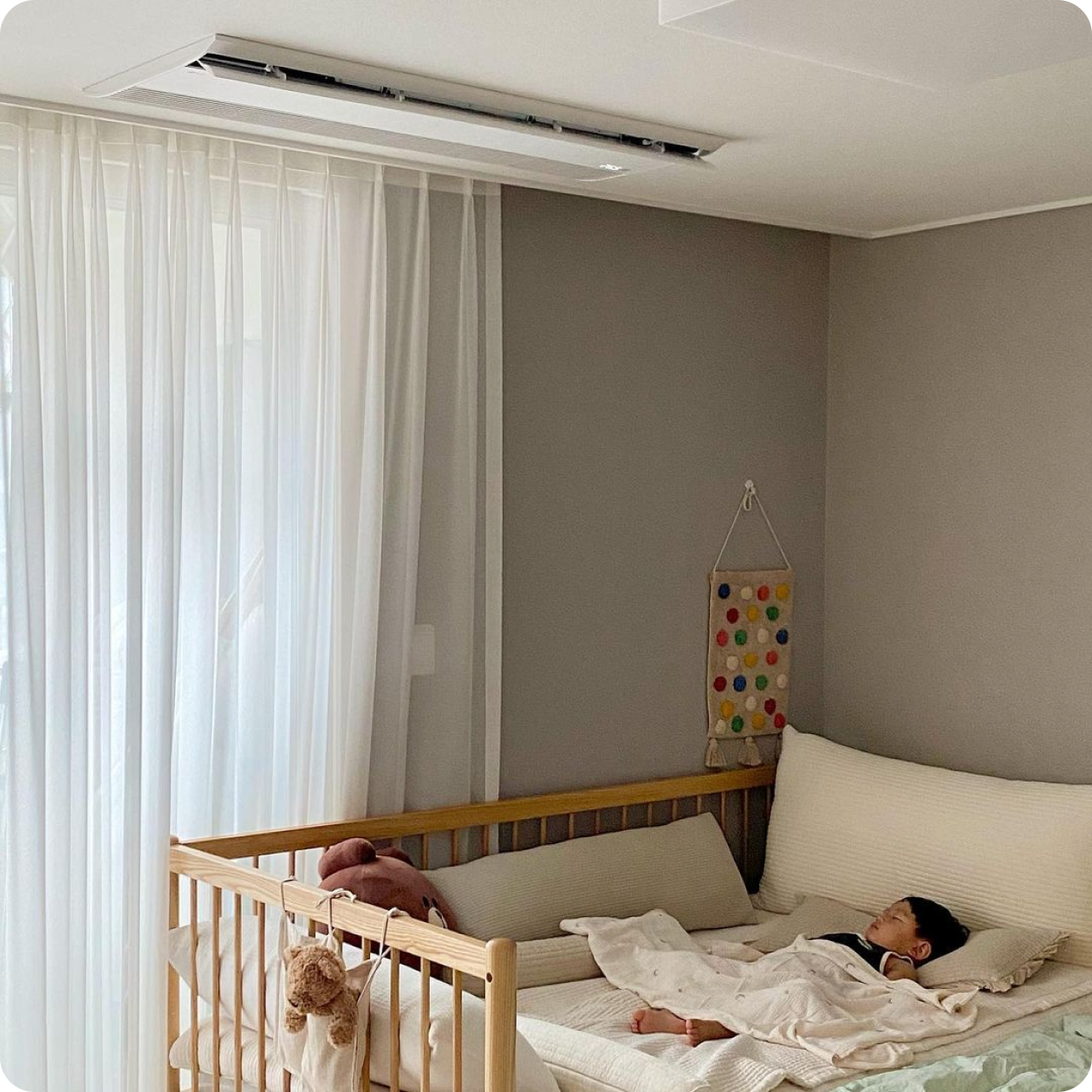 아이가 자고 있는 침실 천장에 설치된 LG 시스템에어컨이 보이며, 주변에 아기 침대와 커튼이 깔끔하게 정돈되어 있다