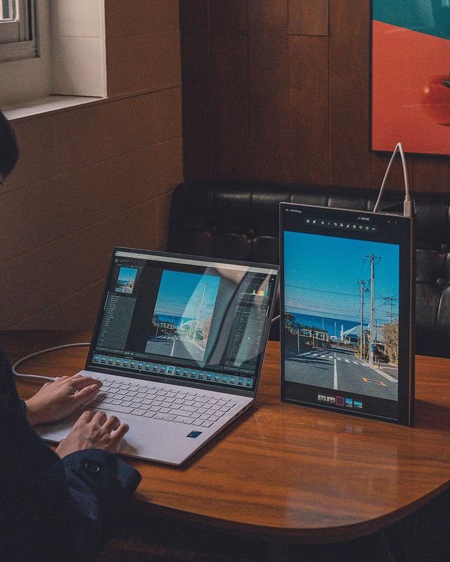 나무 테이블 위 LG 그램 노트북과 세로로 세운 그램+view 포터블 모니터가 연결됨. 노트북에는 사진 편집 프로그램이 열려 있으며, 배경은 나무 패널 벽과 소파, 그림이 어우러진 아늑한 공간임.