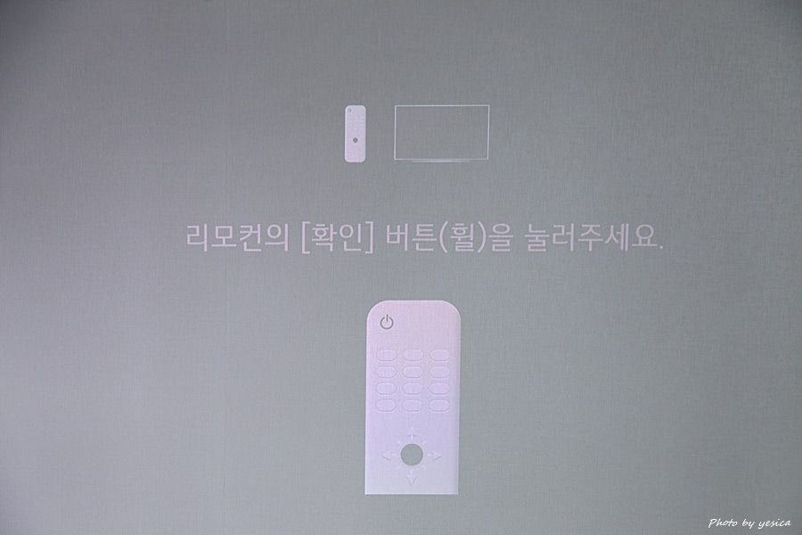 시네빔 큐브 화면에 리모컨 조작 안내 메시지가 표시됨. 확인 버튼(휠)을 눌러주세요라는 문구와 리모컨의 이미지가 함께 나타나 사용법을 쉽게 이해할 수 있도록 돕는 구성임.