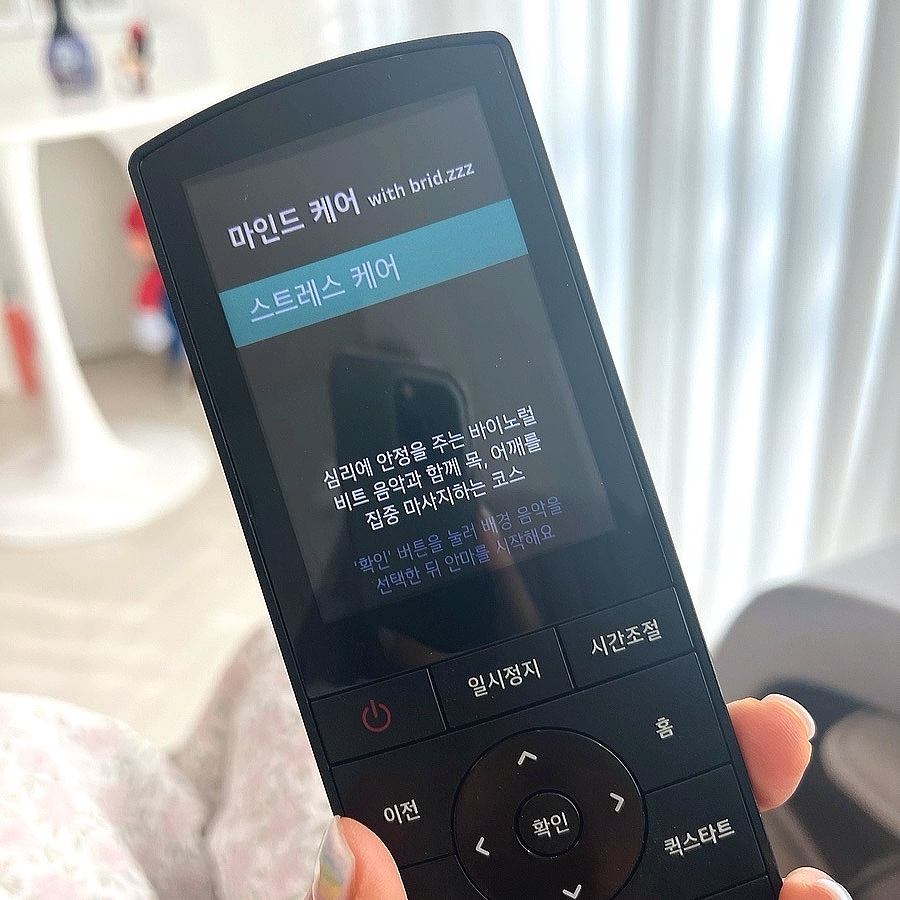 손에_들린_lg_힐링미_mx9_안마의자_리모컨의_화면이_확대되어_있고,_화면에는_마인드_케어_코스의_스트레스_케어가_선택되어_있다._