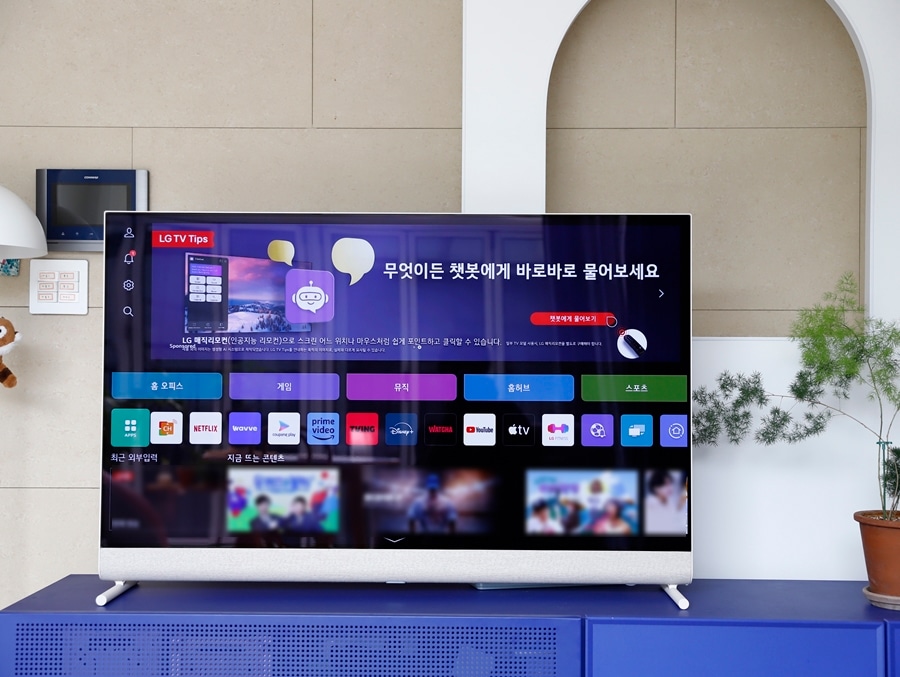 tv가_네이비색_거실장_위에_배치되어_있으며,_화면에는_lg_tv_홈_화면과_콘텐츠_추천_메뉴가_표시됨._배경에는_아치형_인테리어_벽면과_벽걸이_조명,_식물_화분_등이_있음.