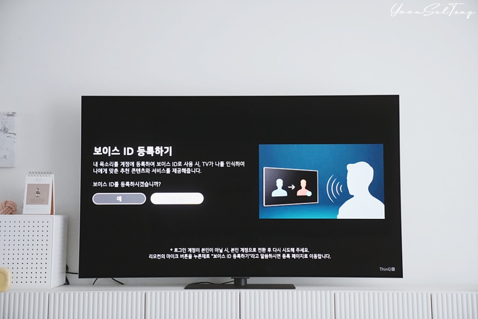 거실_수납장_위에_놓인_tv_화면에_보이스_id_등록_안내가_표시됨._음성_인식을_통한_개인_맞춤_서비스_제공_내용을_포함함._옆엔__캘린더,_장식품_등이_있음.