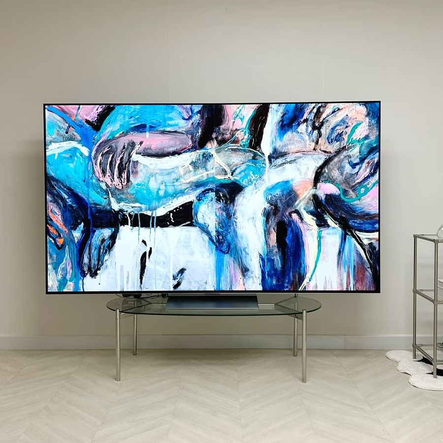tv_화면에_추상적인_그림이_표시되고_있음._화면의_상단과_하단은_물감이_섞여_있는_듯한_색상들이_보임._tv는_유리_테이블_위에_놓여_있음.