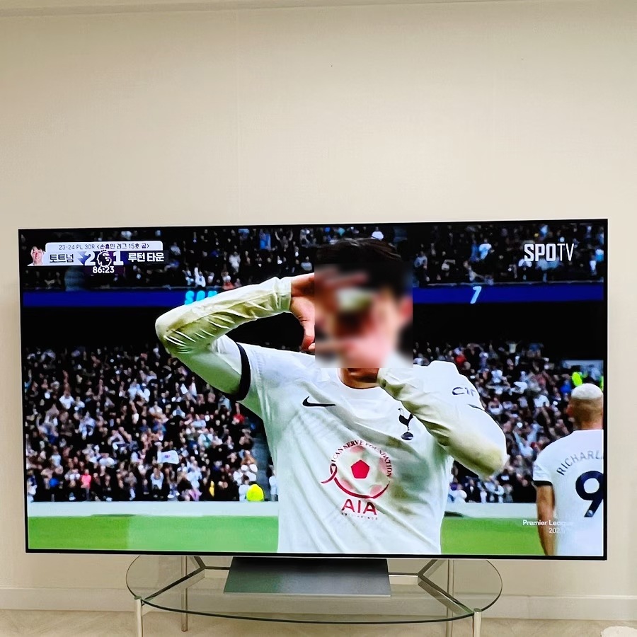 tv_화면에_축구_경기_중_선수들이_득점_후_세리머니를_하는_장면이_표시되고_있음._tv는_유리_테이블_위에_놓여_있음.