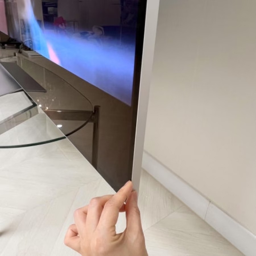 손으로_얇은_베젤의_tv_측면을_잡고_있음._유리_테이블과_바닥이_반사되어_보이며,_tv_화면에는_영상이_재생_중임.