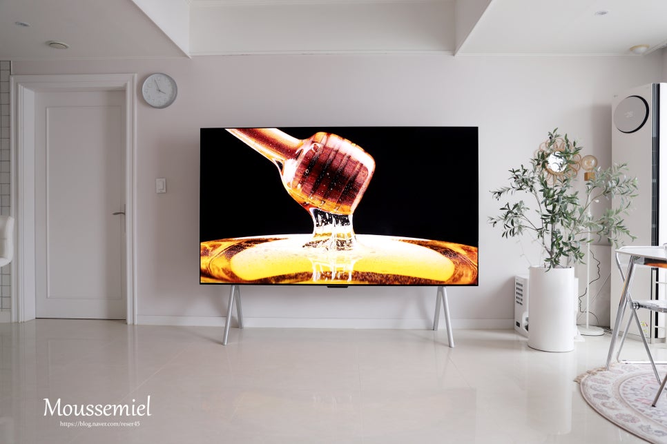 lg_signature_oled_m_tv가_고해상도로_꿀을_흘리는_나무_스푼의_클로즈업_영상을_재생하고_있다._생생한_색감과_깊은_블랙_표현이_강조되며,_거실_인테리어는_깔끔하고_미니멀한_스타일을_유지하고_있다.