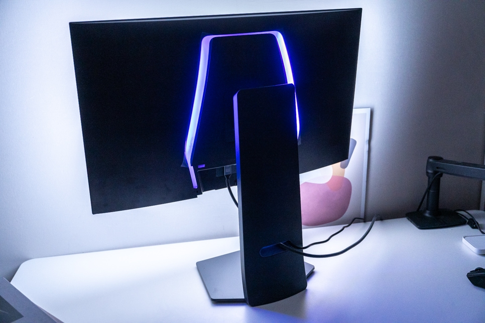 모니터 후면, 은은한 파란색 LED 조명이 돋보이며, 깔끔하게 정리된 케이블과 세련된 스탠드 디자인이 모던한 작업 공간을 연출함.