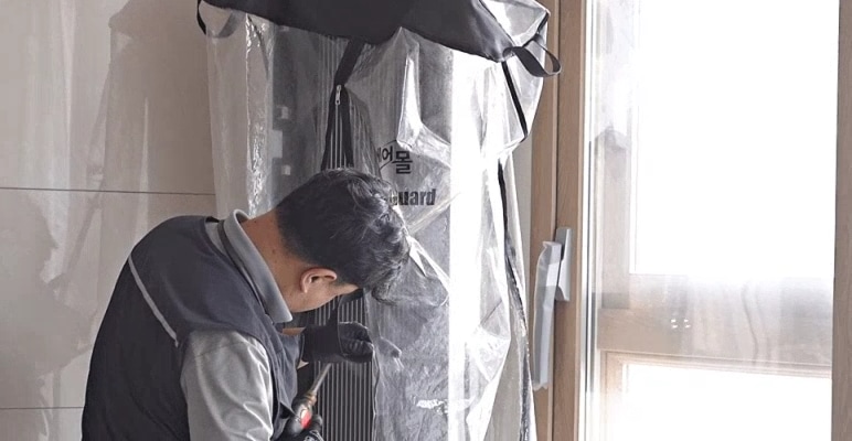 전문 기사가 커버를 씌운 후 에어컨 내부를 고압 세척기로 청소하는 모습. 물이 튀지 않도록 창문 앞에서 꼼꼼하게 작업 중.