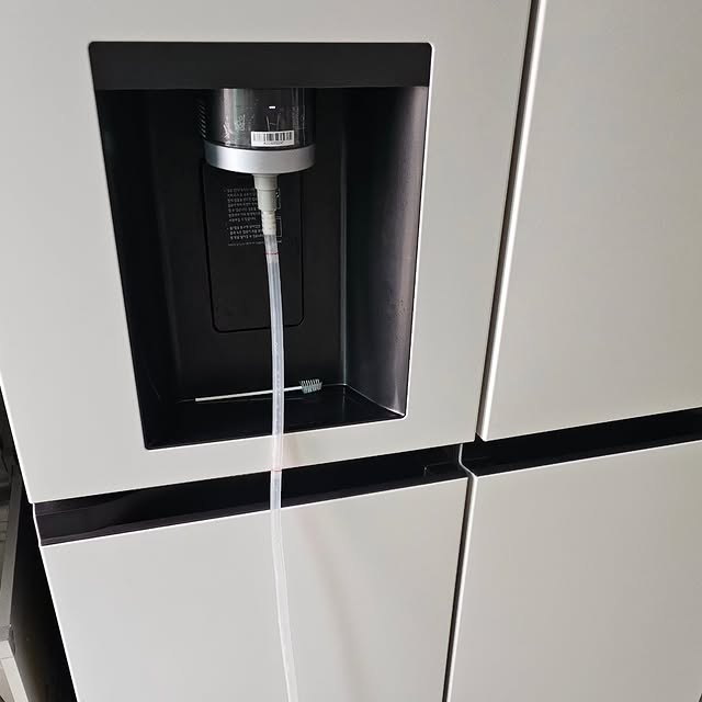 LG 디오스 오브제컬렉션 STEM 얼음정수 냉장고의 정수기 디스펜서 클로즈업 이미지. 정수기 필터가 연결된 상태이며, 투명한 호스를 통해 물이 흐를 준비가 되어 있다.