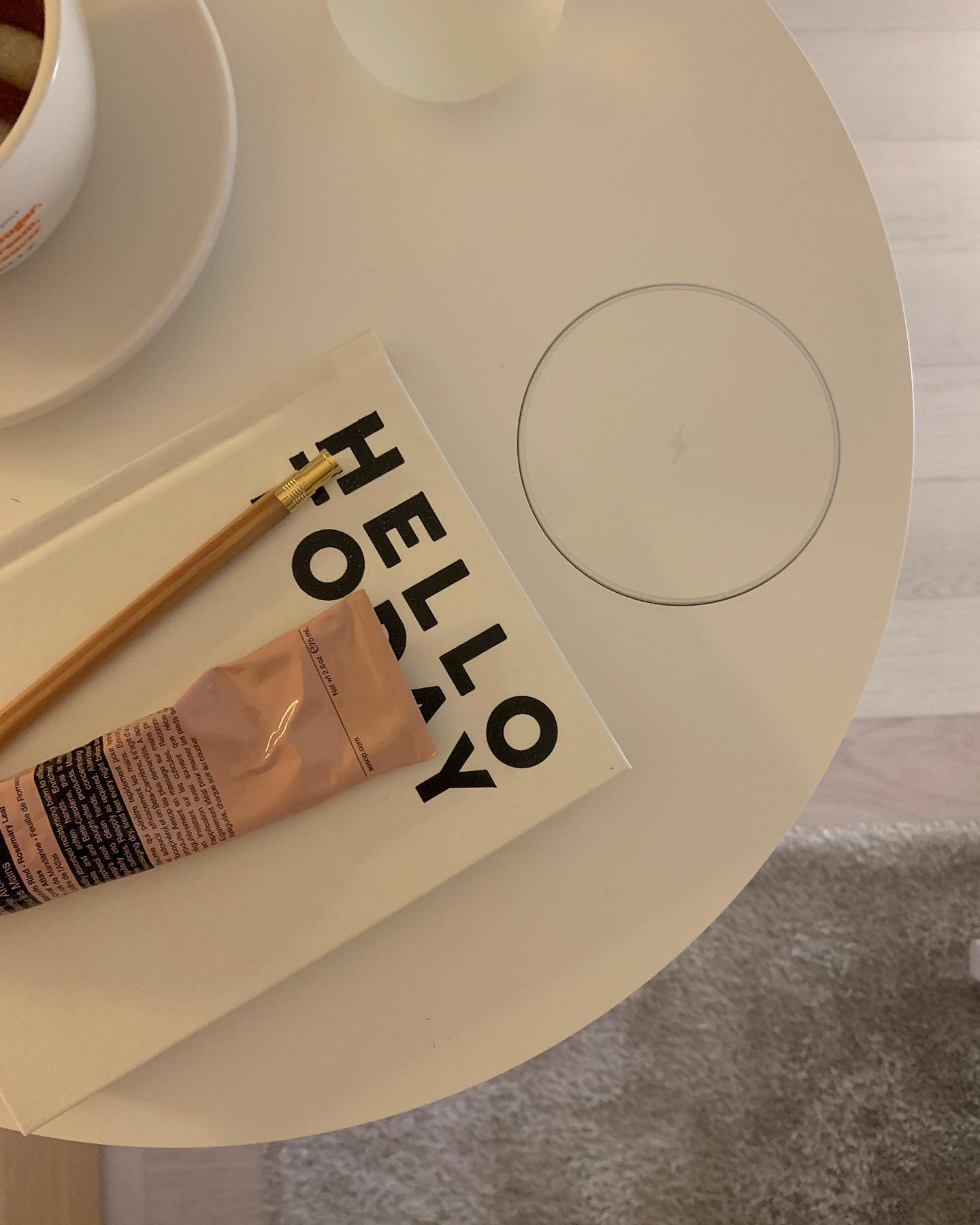 화이트 테이블 위에 'HELLO TODAY'가 적힌 책, 연필, 핸드크림 튜브가 놓여 있으며, 무선 충전 패드가 내장된 깔끔한 디자인