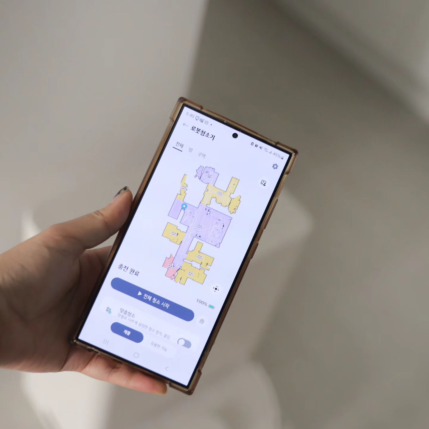 손에 스마트폰을 들고 코드제로 로보킹의 청소 경로를 설정하는 화면을 확인하는 모습임. 앱을 통해 청소 구역을 지정하고 시작할 수 있음.