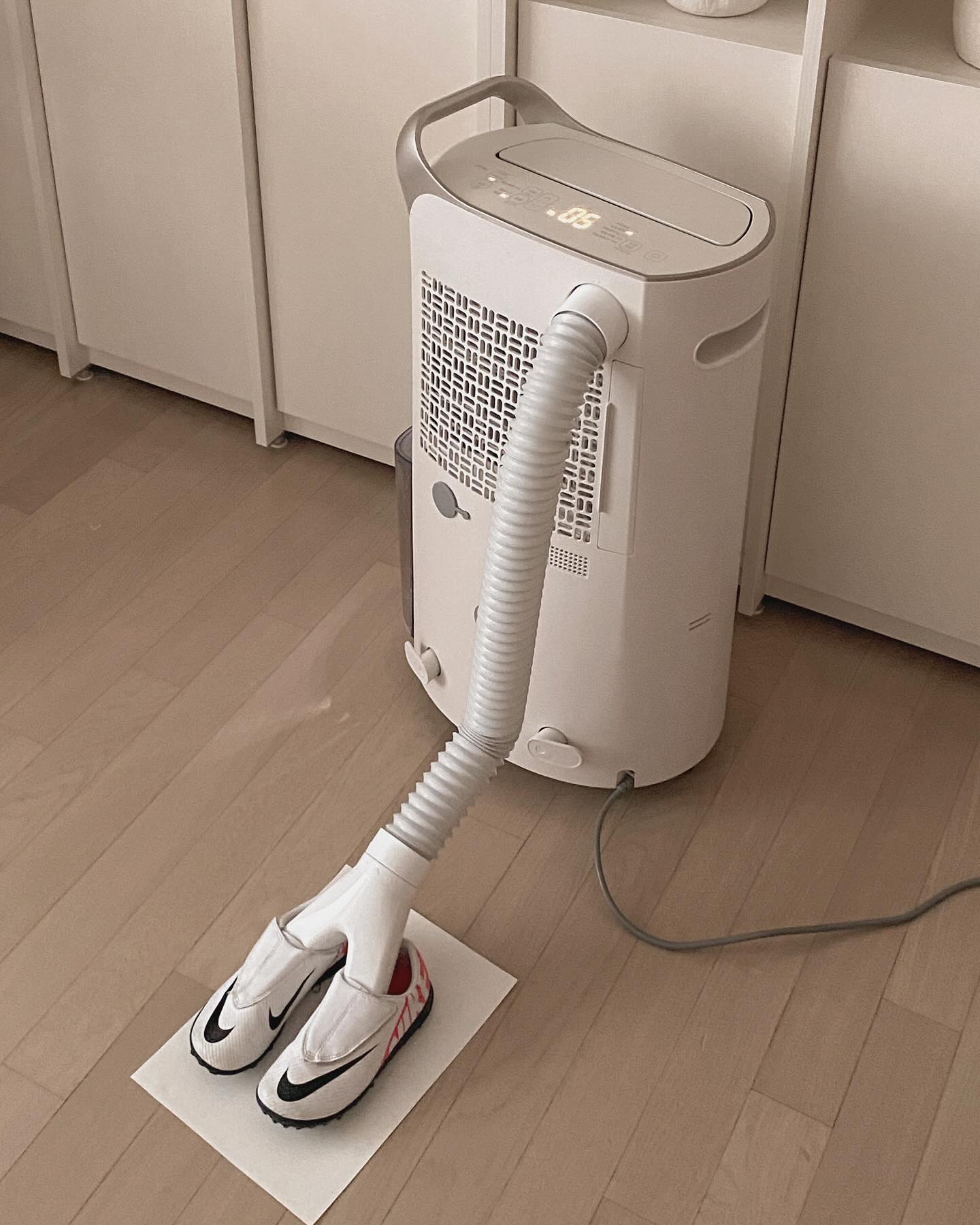 휘센 제습기에 신발 건조 키트를 연결해 운동화를 건조하는 모습. 밝은 우드 톤 바닥과 심플한 수납장이 조화를 이루는 깔끔한 공간임.